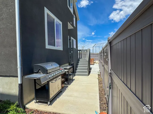 Exterior pathway featuring concrete paving, a dark-toned privacy fence, and an elevated wooden deck with stairs