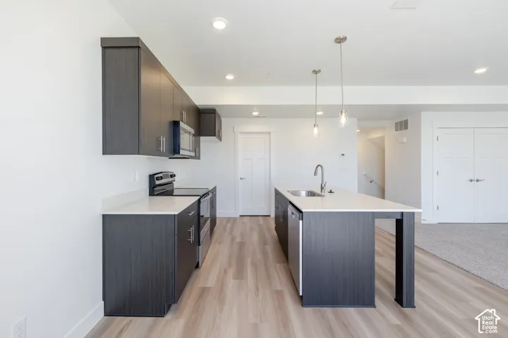 Kitchen featuring dark-toned flat-panel cabinetry, quartz countertops, a central island with an integrated stainless steel sink, recessed lighting, and wood-finish flooring
