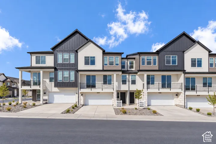 Contemporary multi-unit exterior featuring vertical board-and-batten siding, neutral stucco finishes, stacked stone accents, integrated garage doors, and wrought iron balcony railings