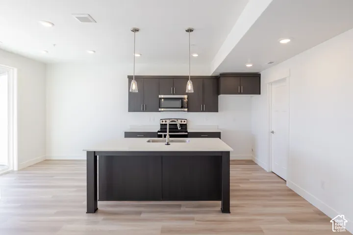 Kitchen featuring a center island with a stone-finish countertop, dark cabinetry, recessed lighting, wood-finish flooring, and pendant lighting