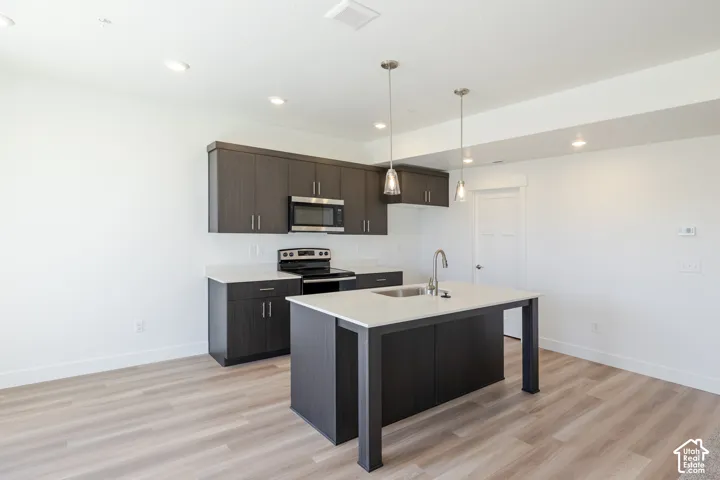 Kitchen featuring dark wood-finish cabinetry, quartz countertops, a central island with an undermount stainless steel sink, recessed lighting, and wood-finish flooring