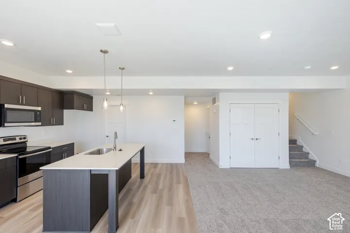Kitchen featuring dark cabinetry, quartz countertops, a central island with an undermount sink, wood-finish flooring, and recessed lighting