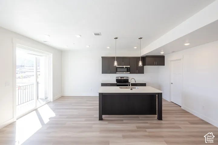 Kitchen featuring dark-toned cabinetry, a center island with quartz countertops, integrated stainless steel appliances, pendant lighting, and wood-finish flooring