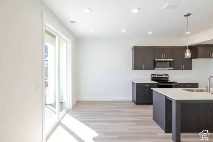 Kitchen featuring dark wood-finish cabinetry, white countertops, stainless steel appliances, wood-finish flooring, and recessed ceiling lighting
