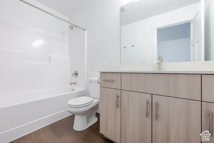 Wood-finish flooring, white tub and shower surround, light wood-tone vanity with brushed nickel hardware, light-colored countertop, and a large vanity mirror