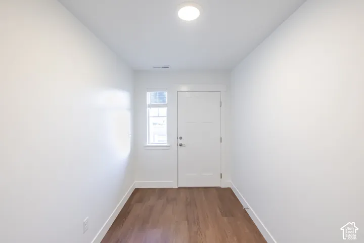 Interior entry with wood-finish flooring, a flush-mount ceiling light, white walls, and a white paneled door with a privacy window
