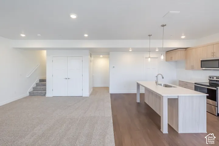 Open-concept living area featuring a kitchen with a large island, stainless steel appliances, and light wood-finish cabinetry