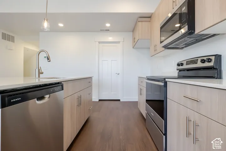 Modern kitchen featuring wood-finish flooring, light-toned cabinetry with contemporary hardware, stainless steel appliances, and a built-in microwave