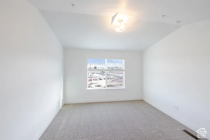 Bright room featuring a single window with blinds, vaulted ceilings, and neutral carpeting