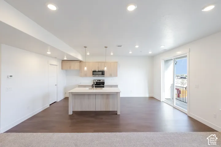 Open concept living space featuring recessed lighting, wood-finish flooring, a kitchen island with pendant lighting, stainless steel appliances, and a sliding glass door to a balcony