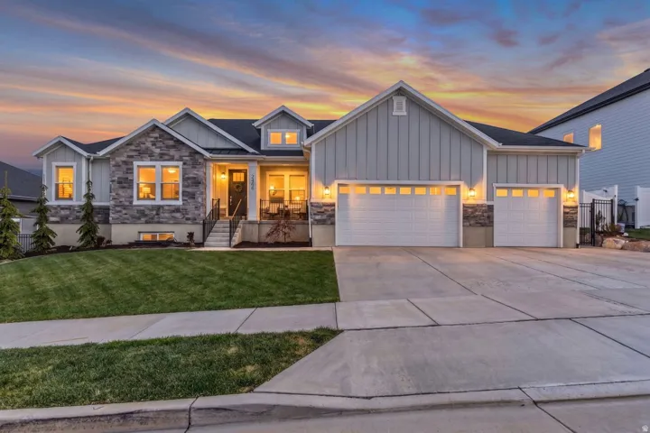 Contemporary residence featuring a stone and board-and-batten facade, a covered front porch, a multi-car driveway, and a manicured lawn