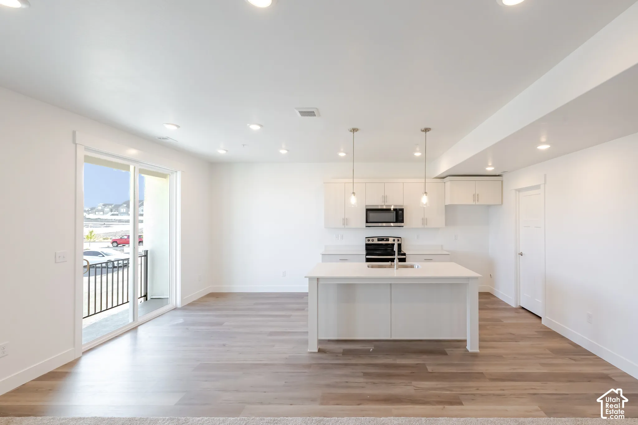 Open-concept living area with wood-finish flooring, white cabinetry, a kitchen island with an undermount sink, and recessed lighting