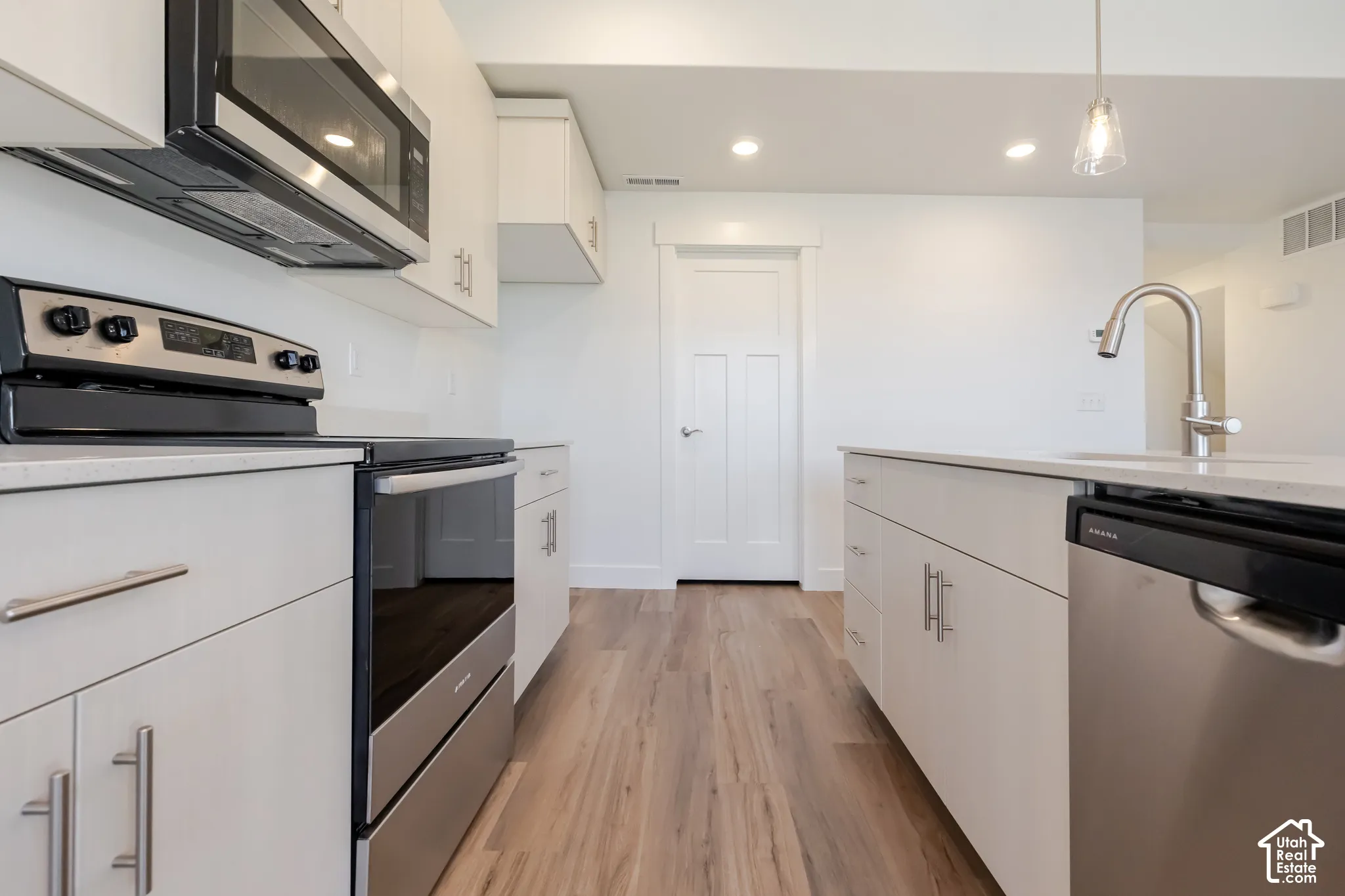 Modern kitchen featuring stainless steel appliances, white cabinetry, a kitchen island with sink, quartz countertops, and wood-finish flooring