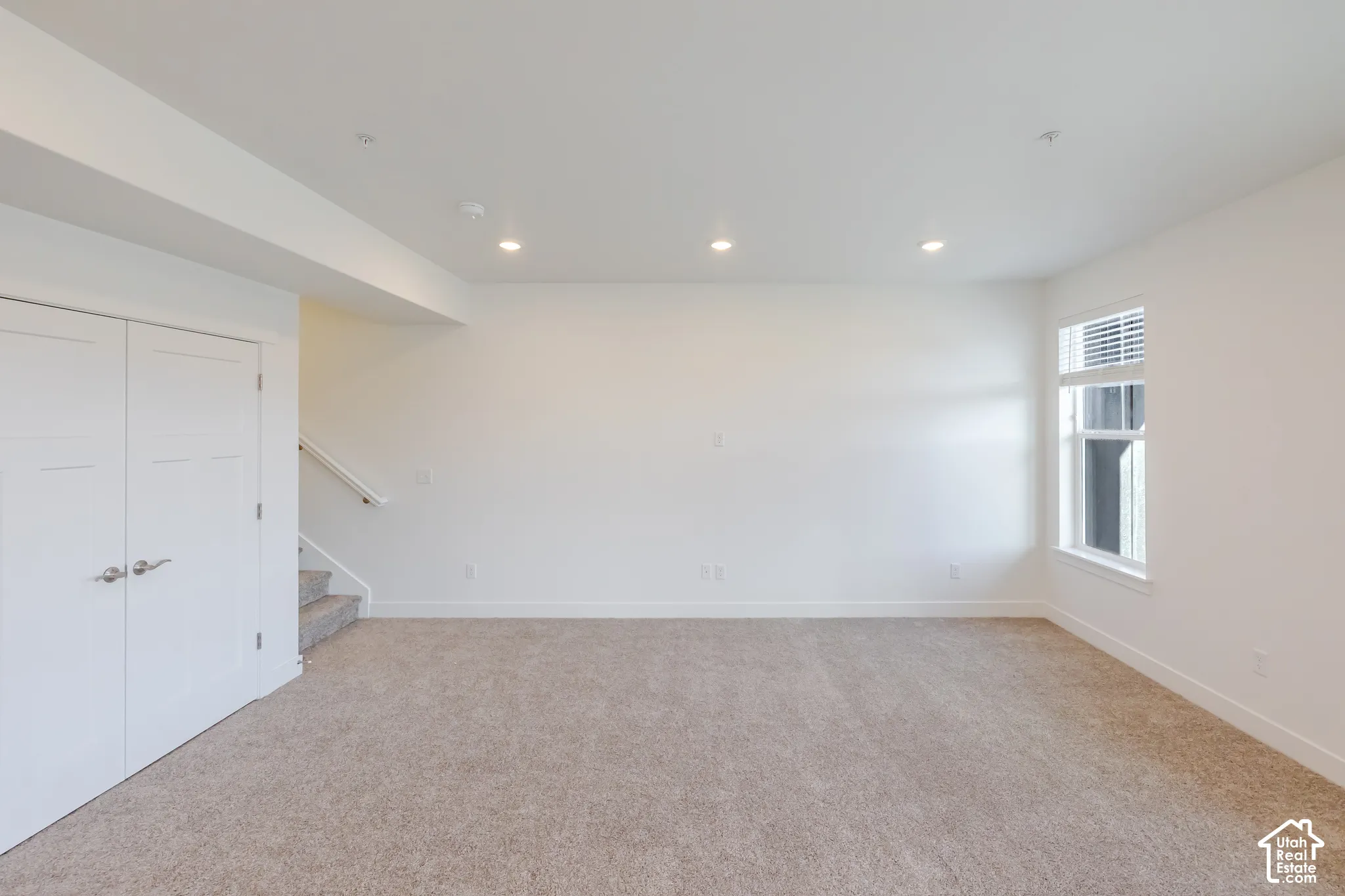 Neutral tone carpeting, recessed lighting, white interior doors with satin nickel hardware, white window trim, and a staircase with a white handrail