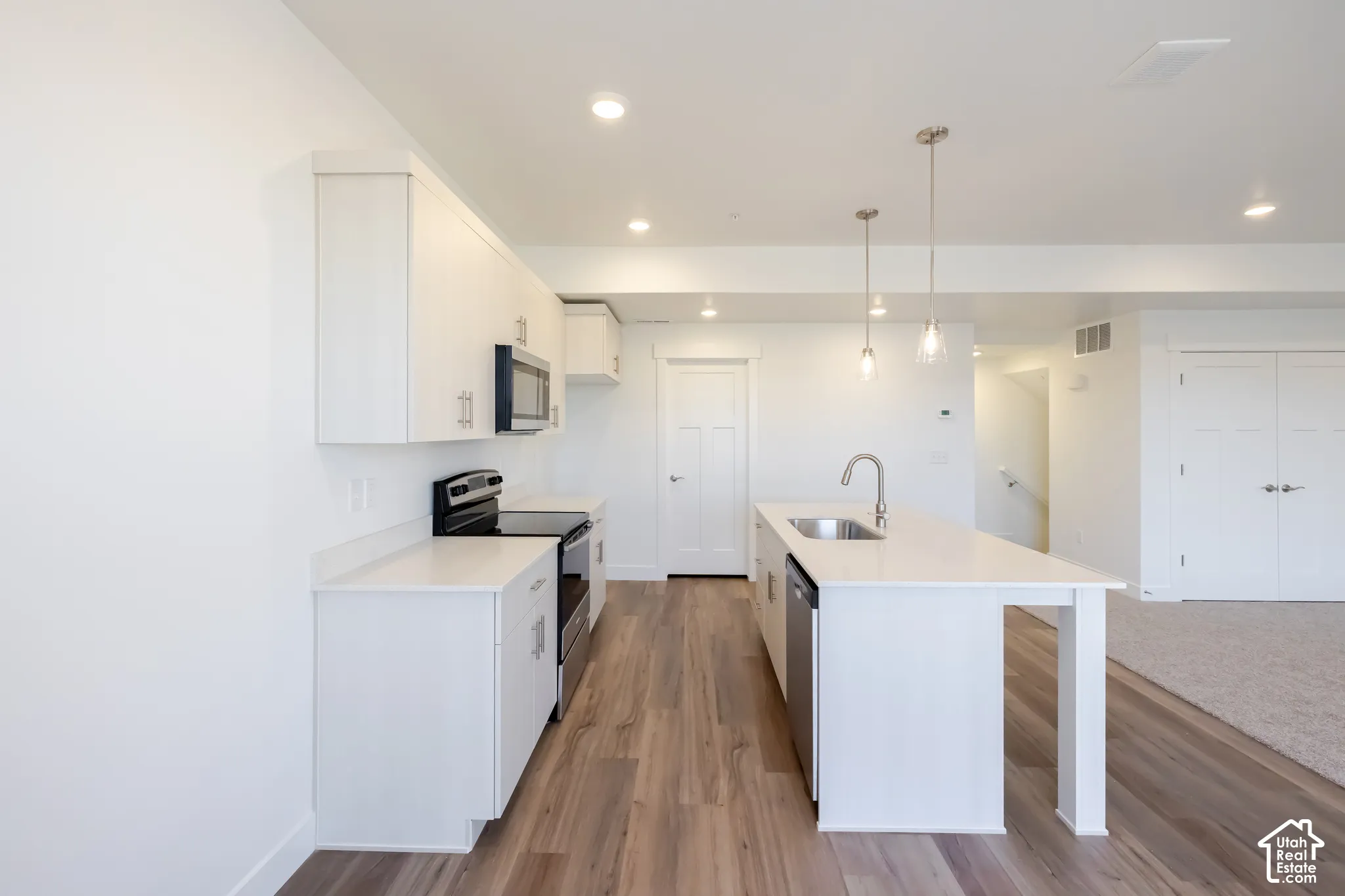 Kitchen with white cabinetry, stainless steel appliances, wood-finish flooring, and a central island with a sink and pendant lighting