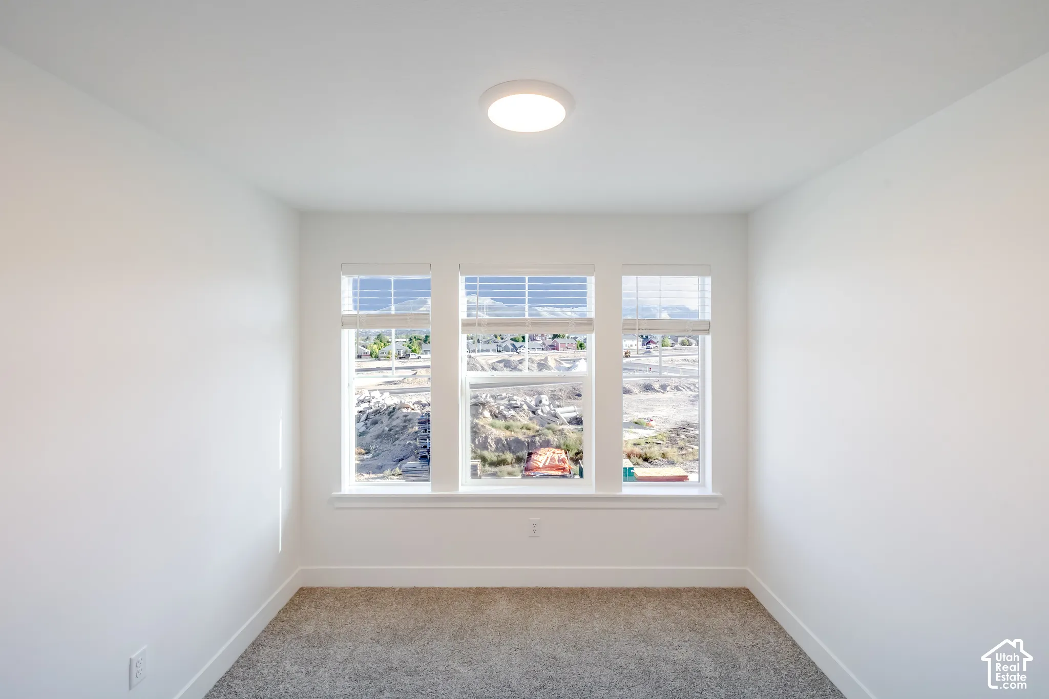 Triple window unit with white trim, flush-mount ceiling light, and wall-to-wall carpeting