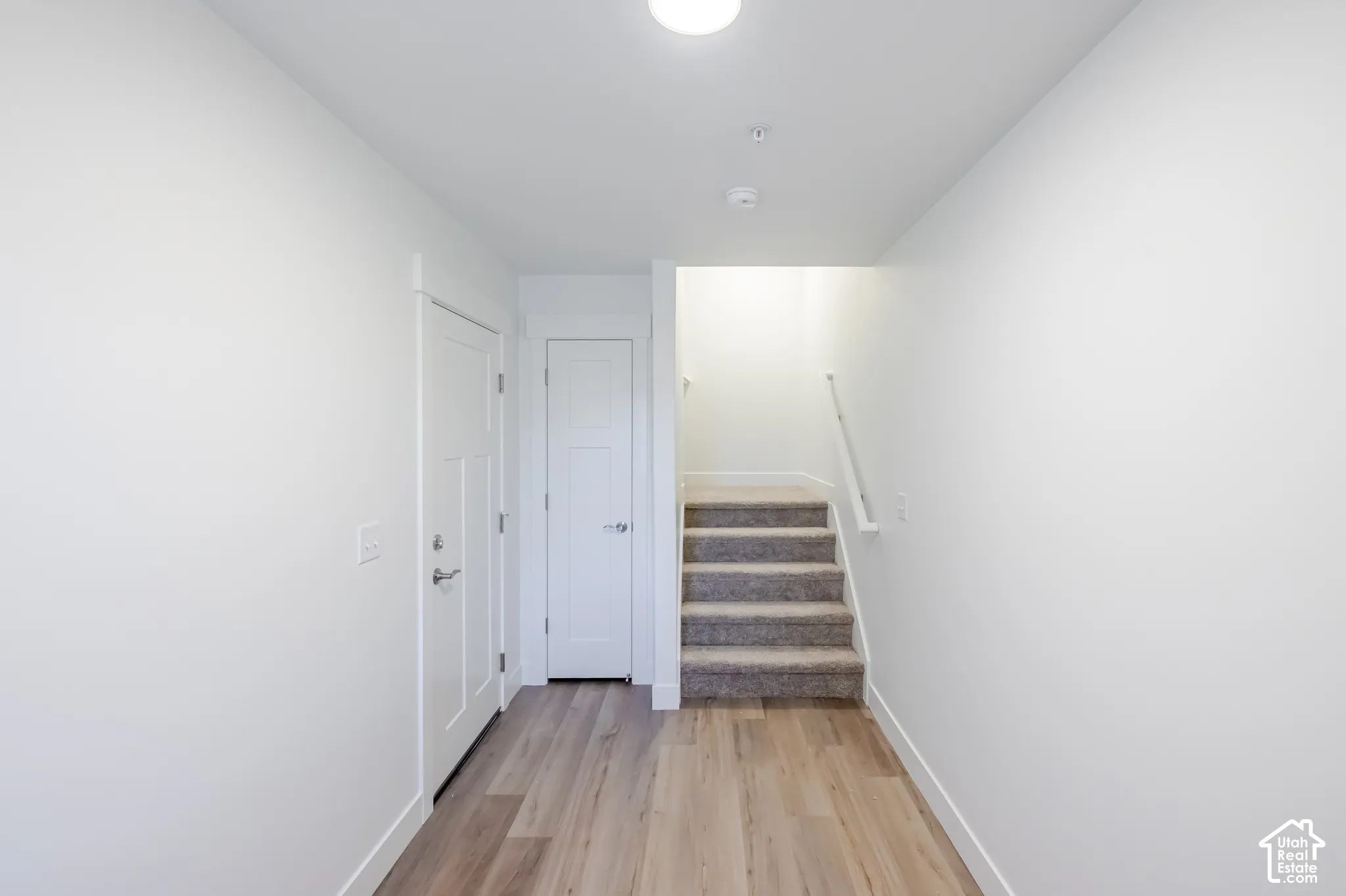 Recessed lighting, wood-finish flooring, white paneled doors, and carpeted stairs with a white handrail