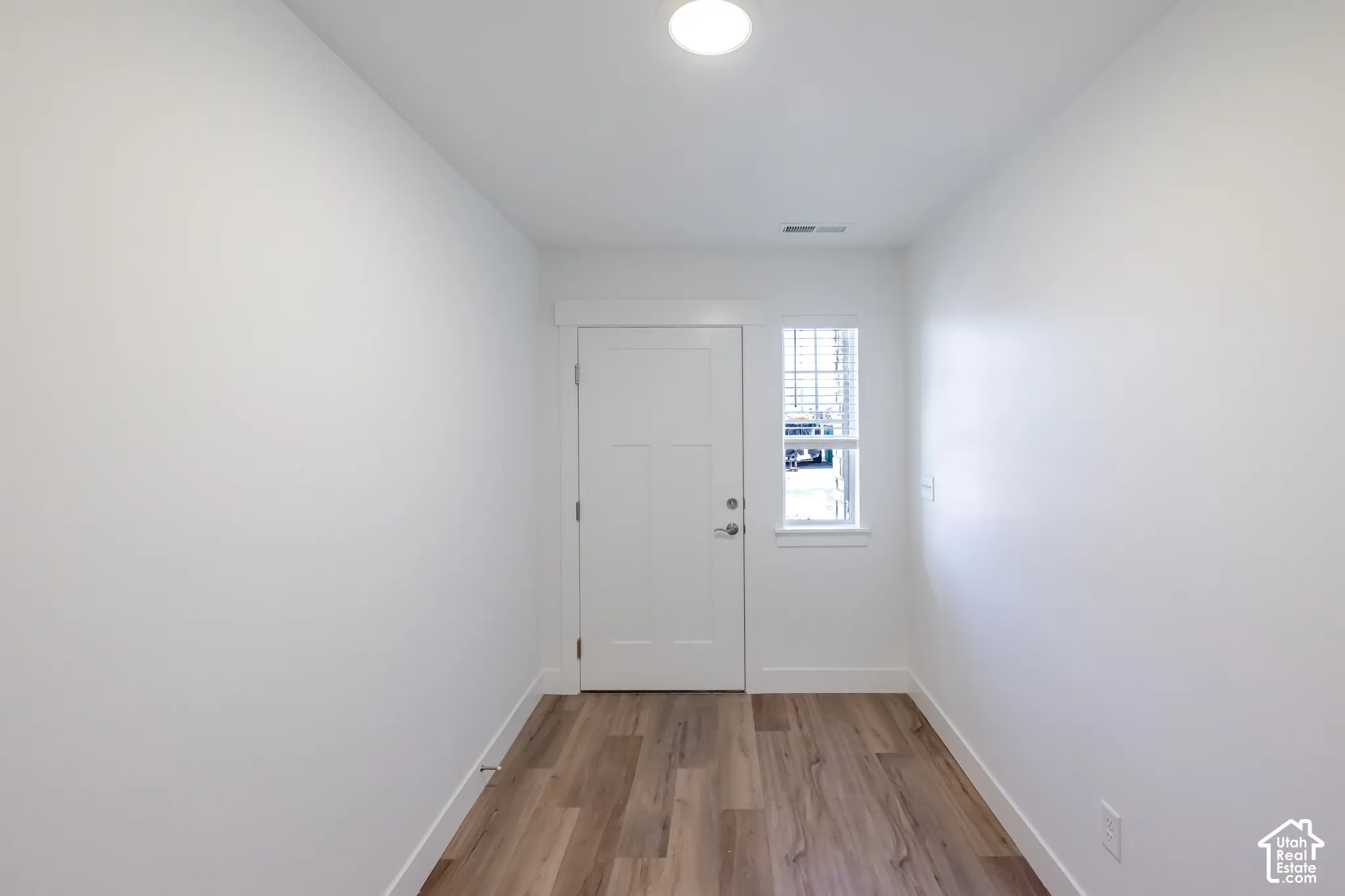 Wood-finish flooring, white walls, and a front entry door with an adjacent window