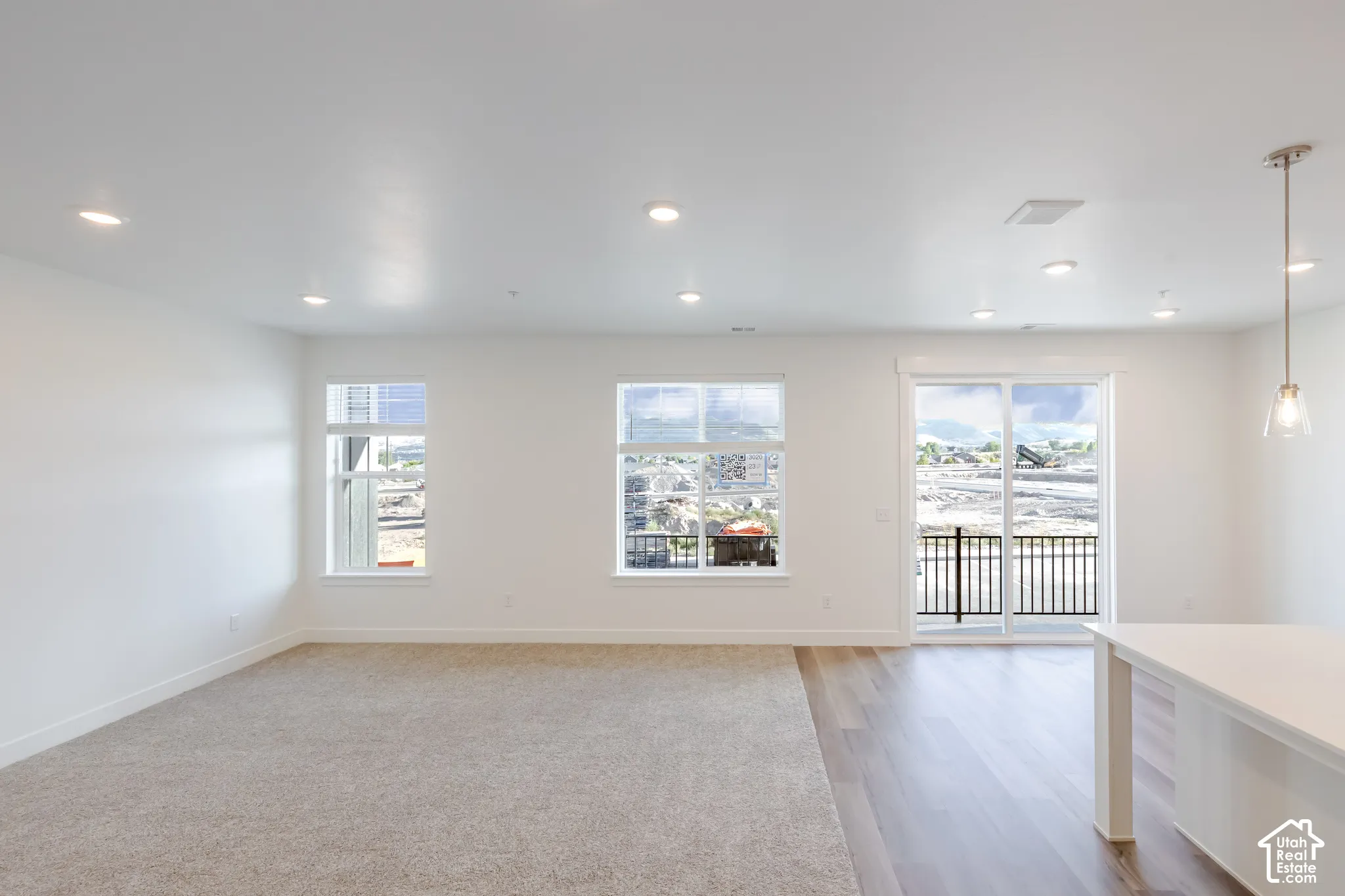 Recessed ceiling lighting, carpet and wood-finish flooring, multiple windows, a sliding glass door, and a kitchen island with pendant lighting