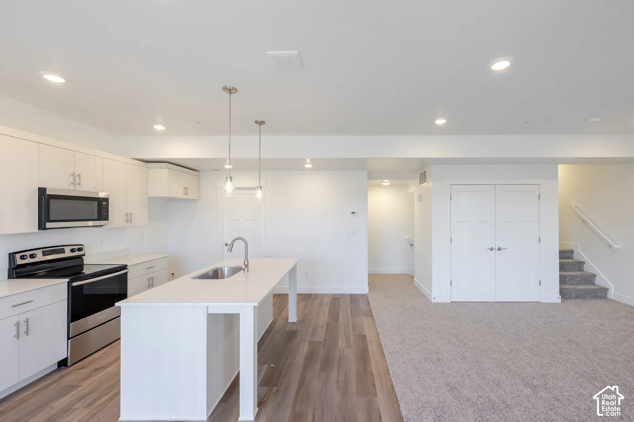 Contemporary kitchen featuring white cabinetry, stainless steel appliances, a center island with sink, pendant lighting, and wood-finish flooring