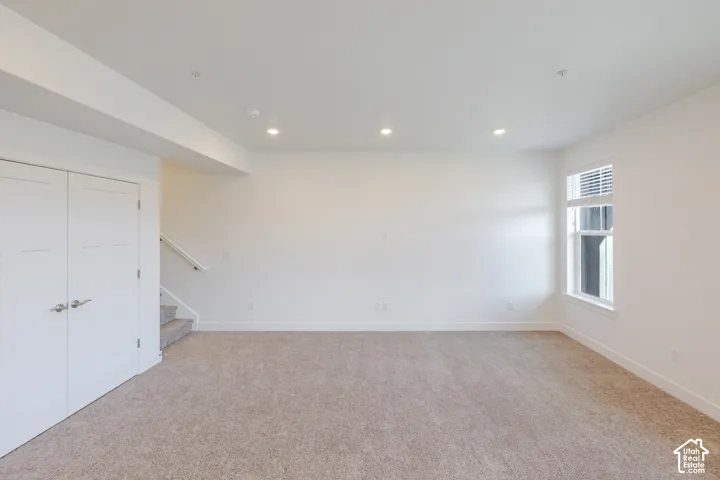 Neutral tone carpeting, recessed lighting, white interior doors with satin nickel hardware, white window trim, and a staircase with a white handrail