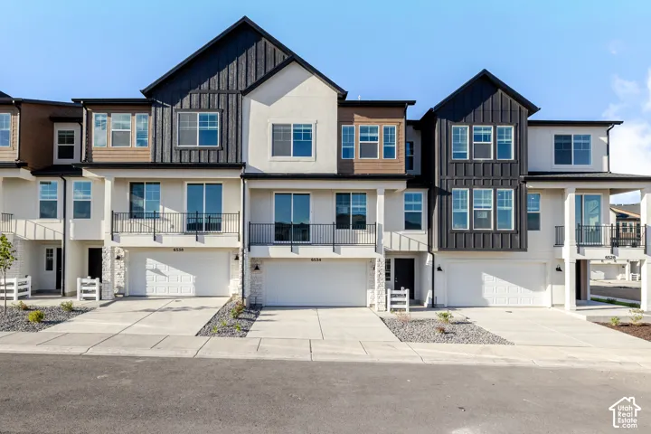 Modern townhome exterior featuring white stucco, dark vertical siding, multiple balconies with black railings, and attached garages
