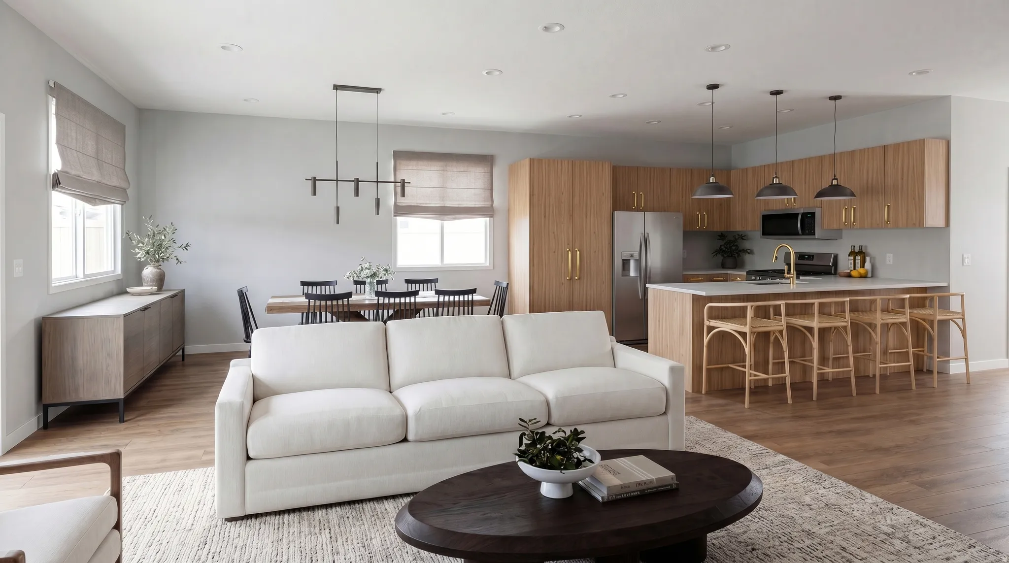 Open-concept living area featuring wood-finish flooring throughout, a modern kitchen with light wood cabinetry, stainless steel appliances, and a central island with bar seating