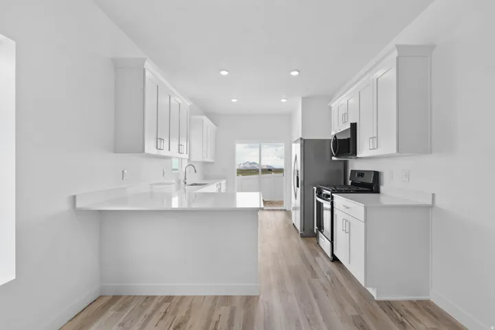 Bright kitchen featuring white shaker cabinetry, light countertops, wood-finish flooring, and recessed lighting