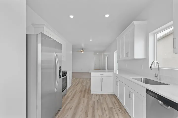 Modern kitchen featuring light wood-finish flooring, white shaker-style cabinetry, and light-toned countertops