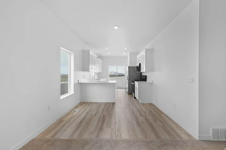 Modern kitchen featuring wood-finish flooring, white cabinetry, integrated stainless steel appliances, a white countertop, and a contemporary sink with a gooseneck faucet