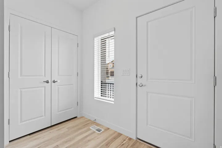 Wood-finish flooring with white baseboards, a white paneled entry door, a window with horizontal blinds, and double paneled closet doors
