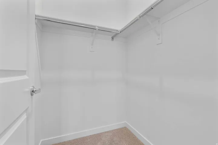 Walk-in closet featuring light-colored carpeting, white baseboards, and a chrome hanging rod
