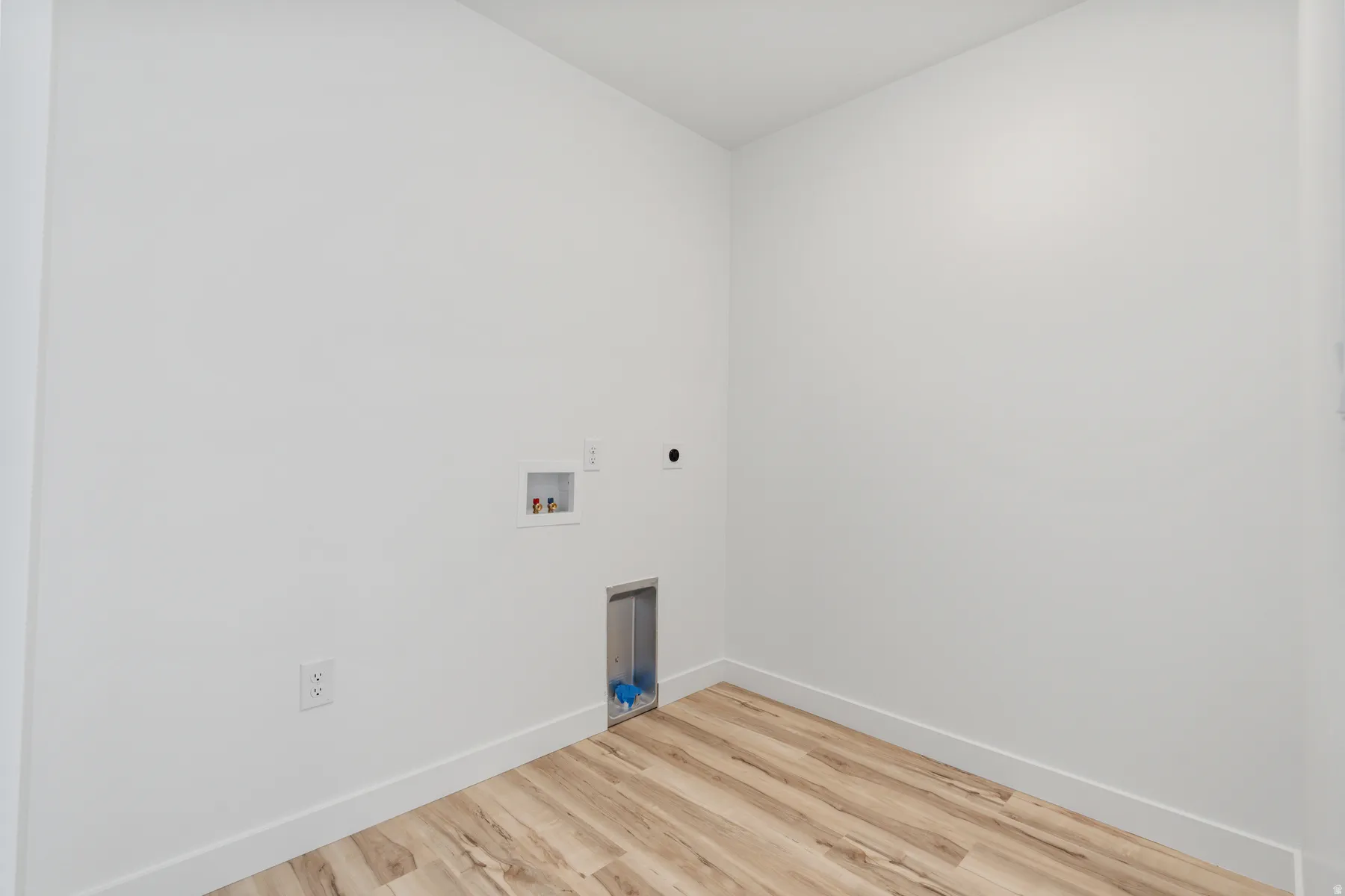 Utility room featuring bright white walls, wood-finish flooring, and essential appliance hookups