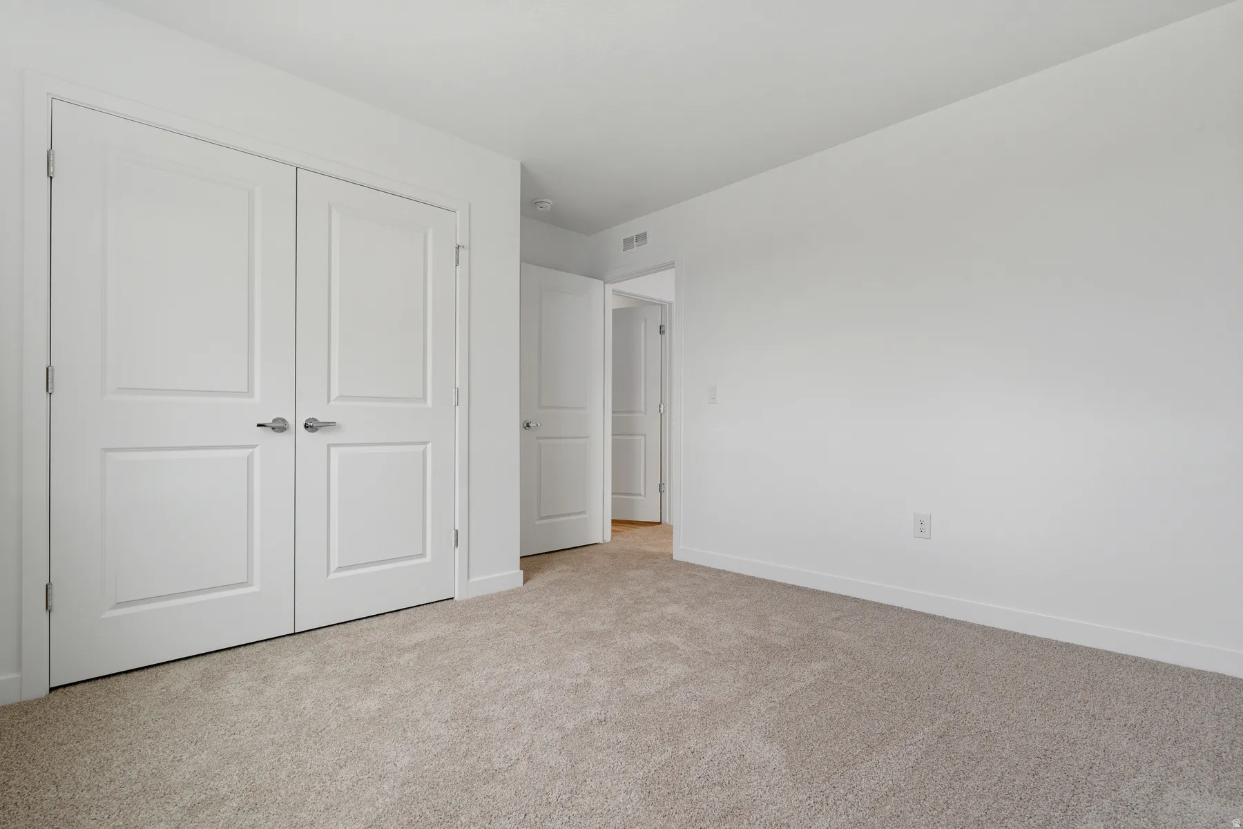 Bedroom featuring neutral carpeting, white walls, and a pair of white paneled doors with brushed nickel hardware