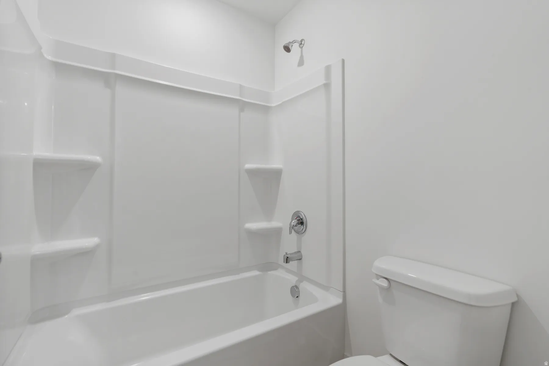 White bathtub with an integrated shower surround featuring built-in shelving, chrome fixtures, and a coordinating toilet