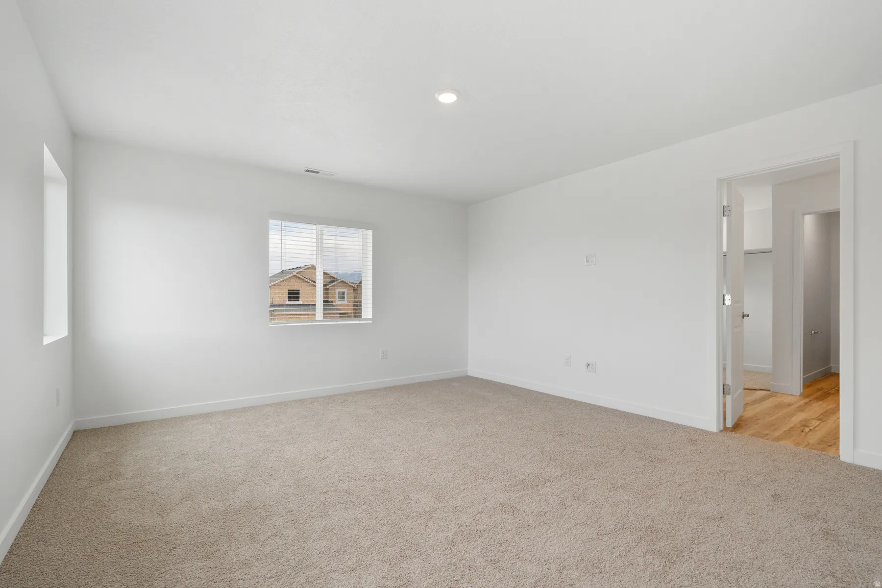 Spacious room featuring neutral carpet flooring, recessed ceiling lighting, and two windows with blinds