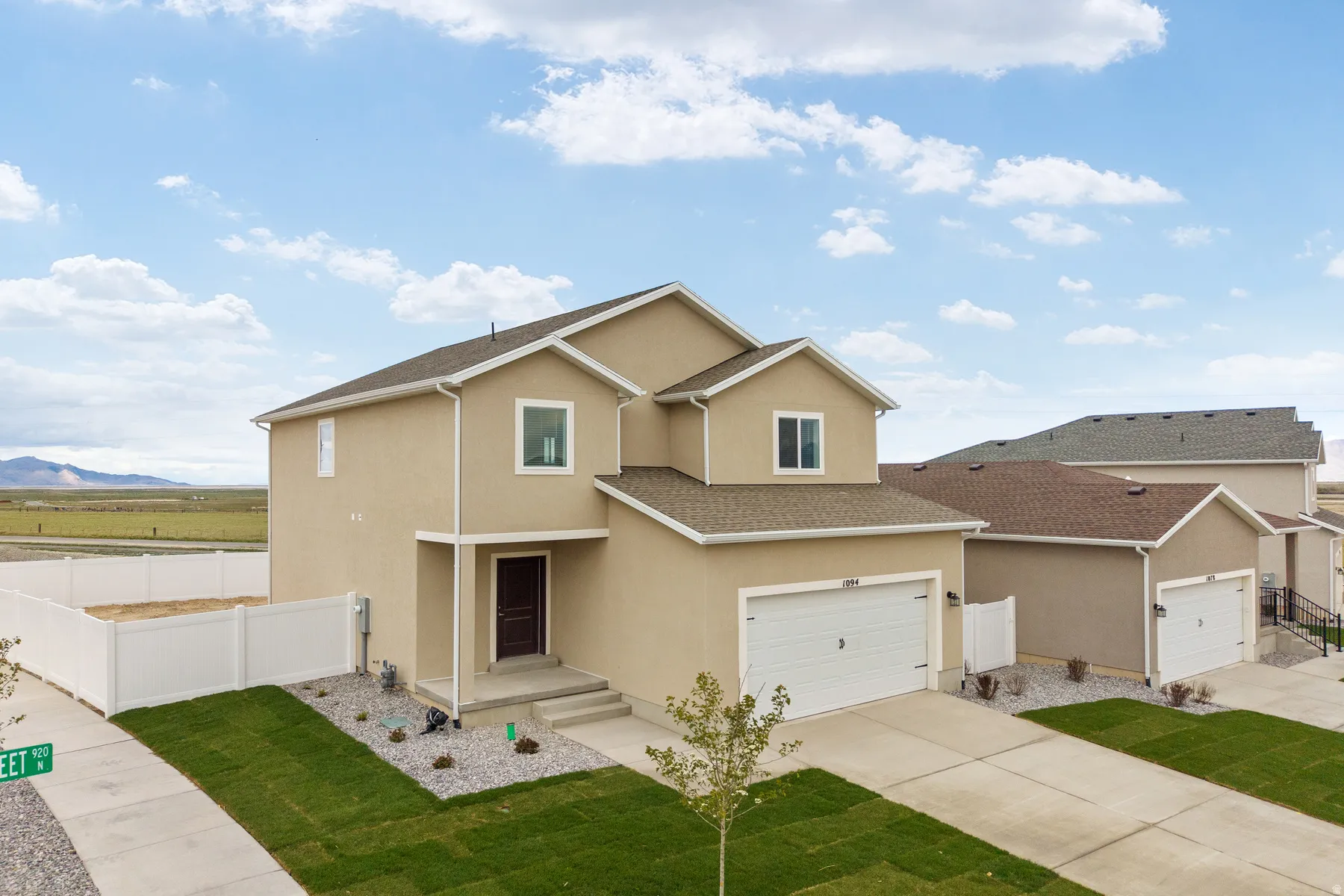 Contemporary stucco exterior featuring a two-car garage, dark wood-finish front door, and established green lawn