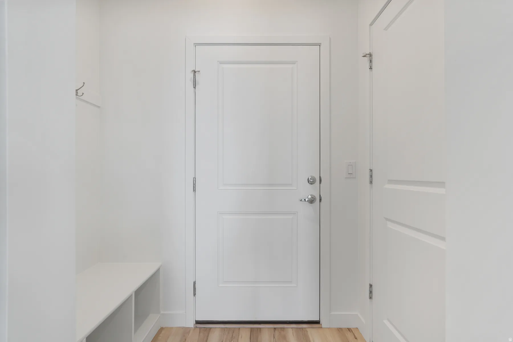 Entryway featuring a built-in bench with storage, wood-finish flooring, and white paneled doors