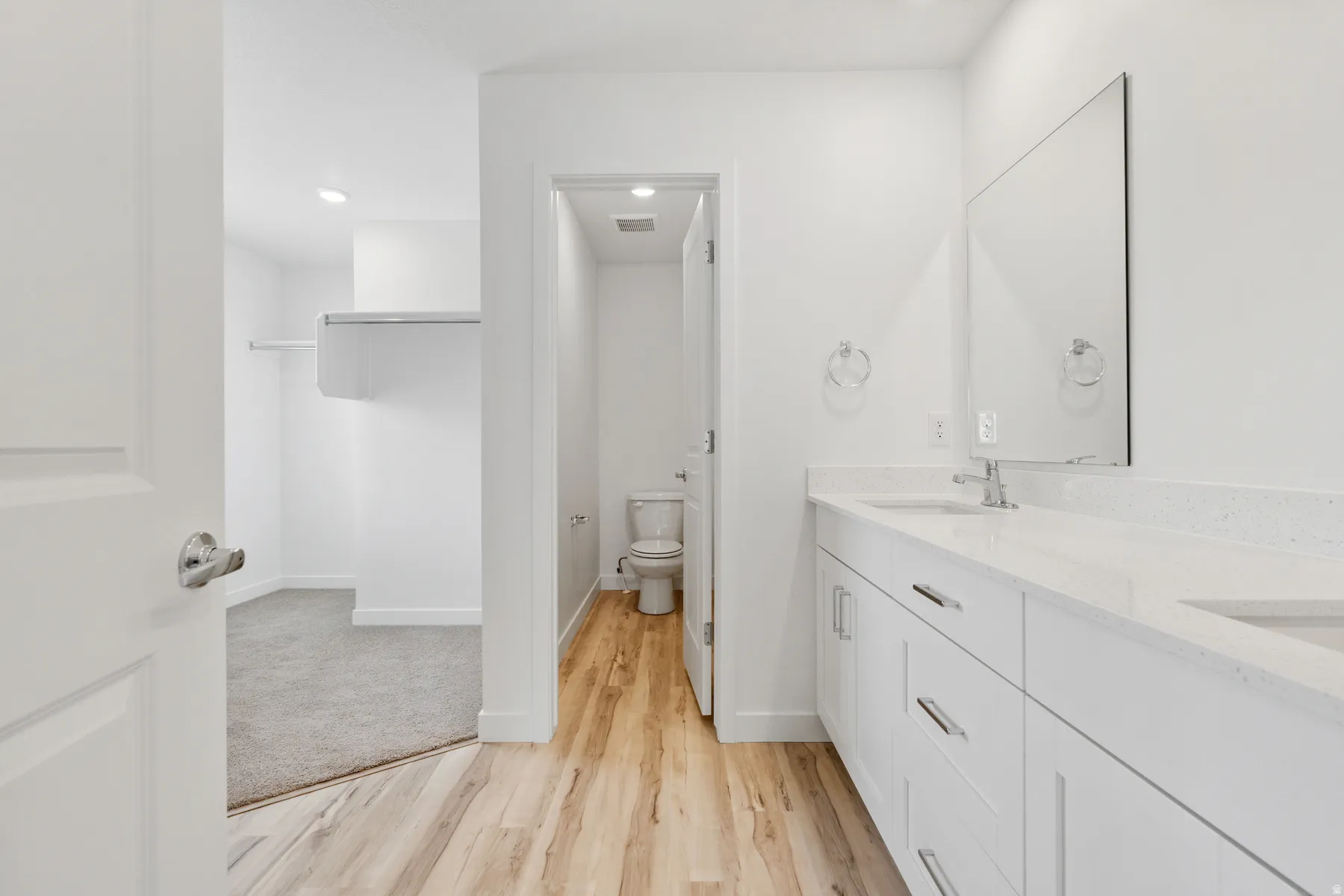 Bathroom vanity with dual sinks, white cabinetry, and a large wall-mounted mirror