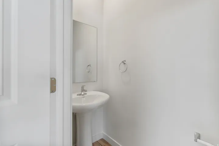 Pedestal sink with chrome faucet, complemented by a rectangular wall mirror and white painted walls