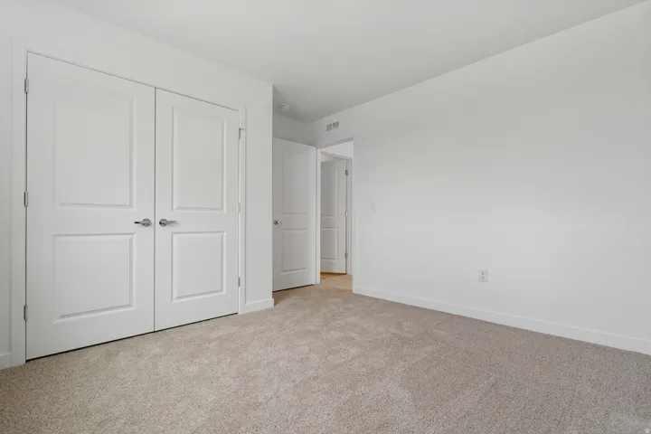 Bedroom featuring neutral carpeting, white walls, and a pair of white paneled doors with brushed nickel hardware