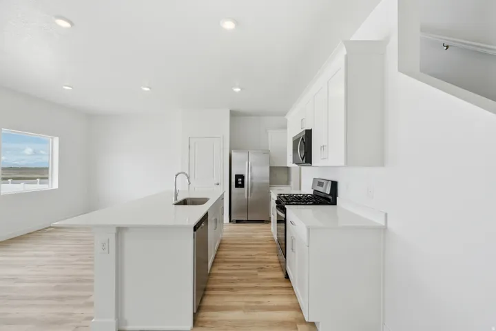 Bright kitchen featuring an expansive island with an integrated sink and dishwasher, white cabinetry, integrated stainless steel appliances, and wood-finish flooring