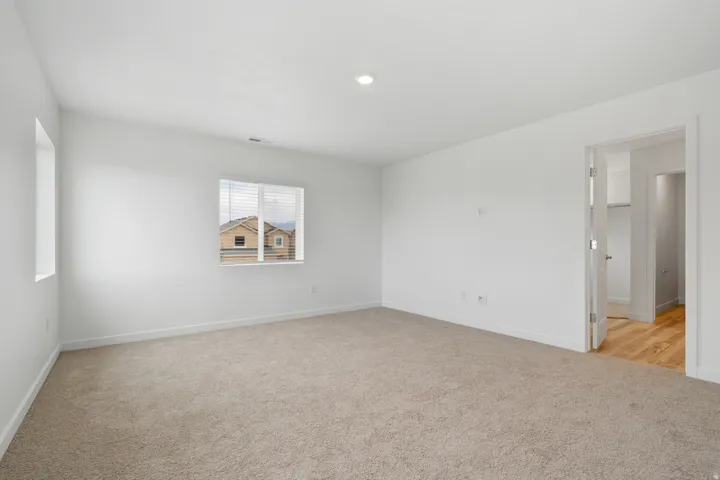 Spacious room featuring neutral carpet flooring, recessed ceiling lighting, and two windows with blinds