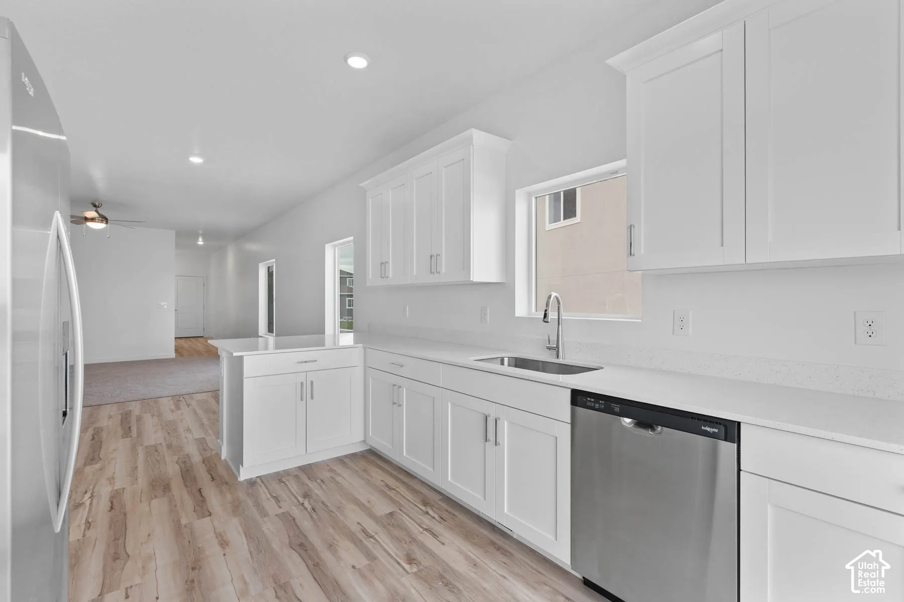 White shaker cabinetry, light-toned wood-finish flooring, stainless steel appliances, recessed lighting, and a kitchen island