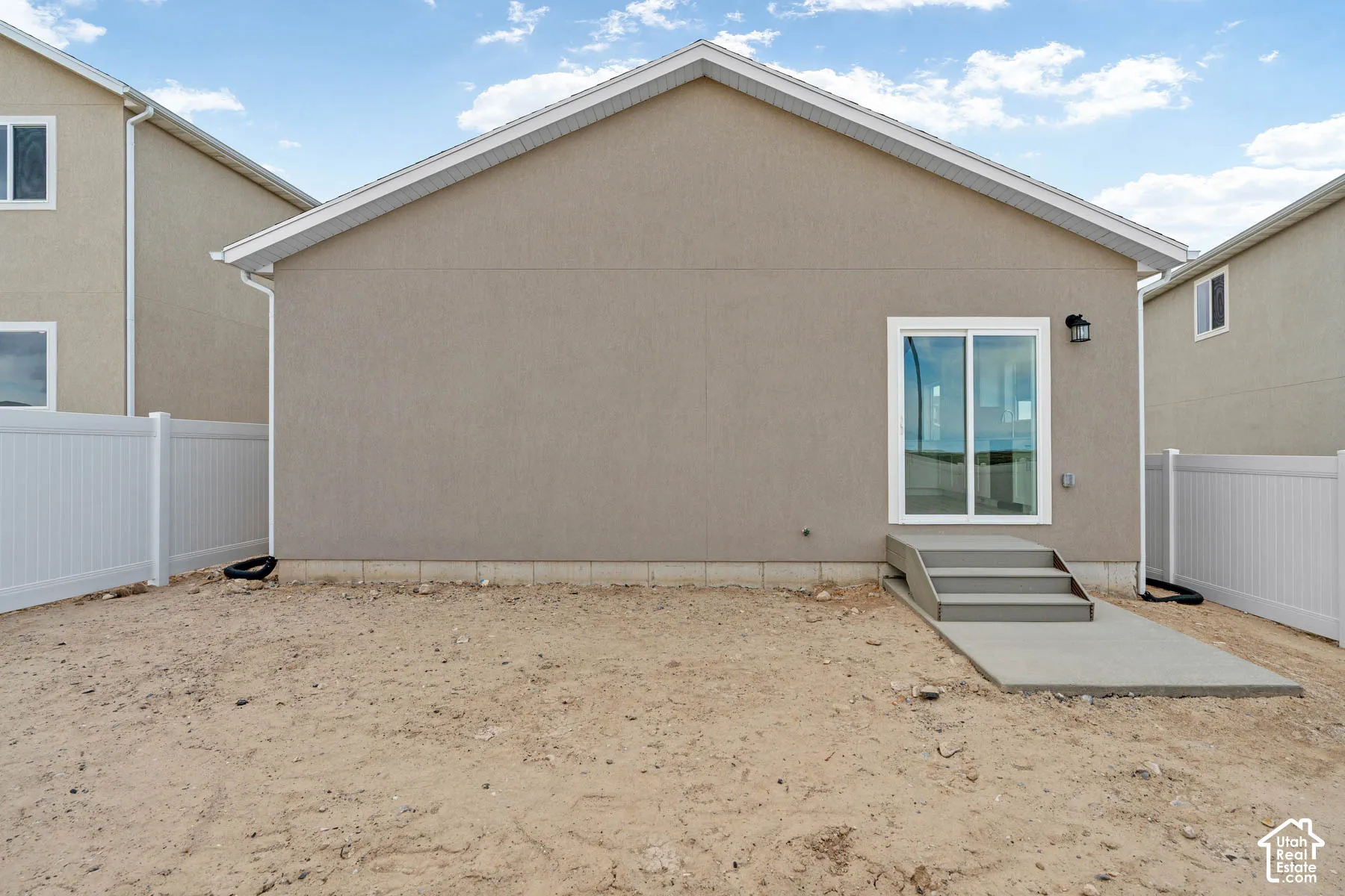 Stucco exterior with white trim, featuring a sliding glass door and concrete steps leading to a concrete patio