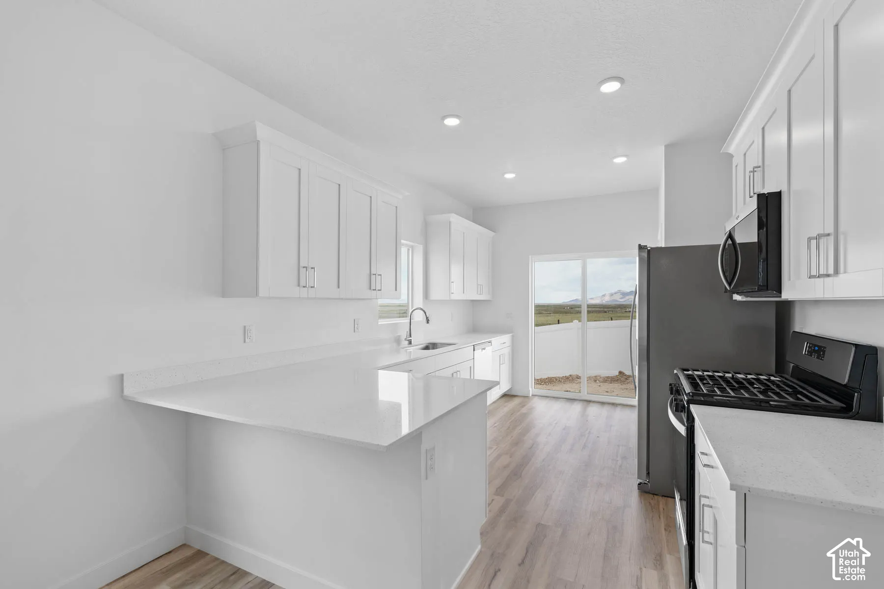 White shaker cabinetry, light-toned wood-finish flooring, recessed lighting, and a stainless steel sink with a gooseneck faucet