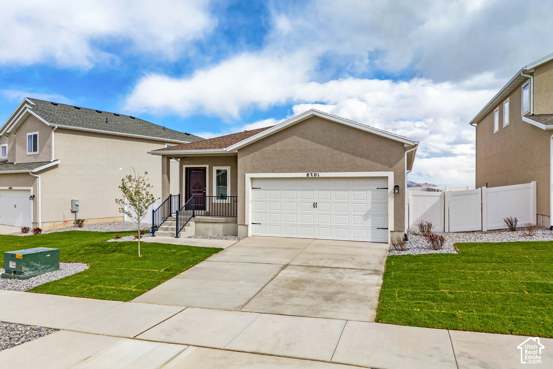 Stucco exterior with a two-car garage, concrete driveway, and covered front porch with railings