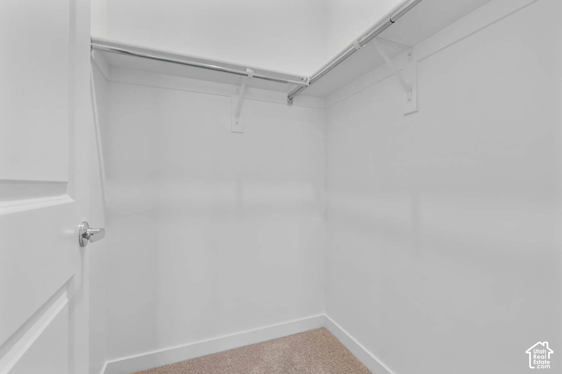 White painted walls, built-in shelving, chrome hanging rods, and carpet flooring