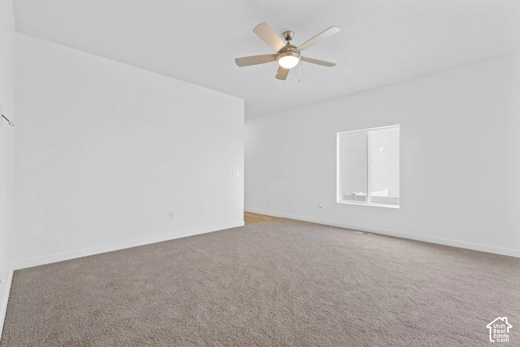 Expansive room with neutral carpeting, white wall finishes, and a ceiling fan with integrated lighting