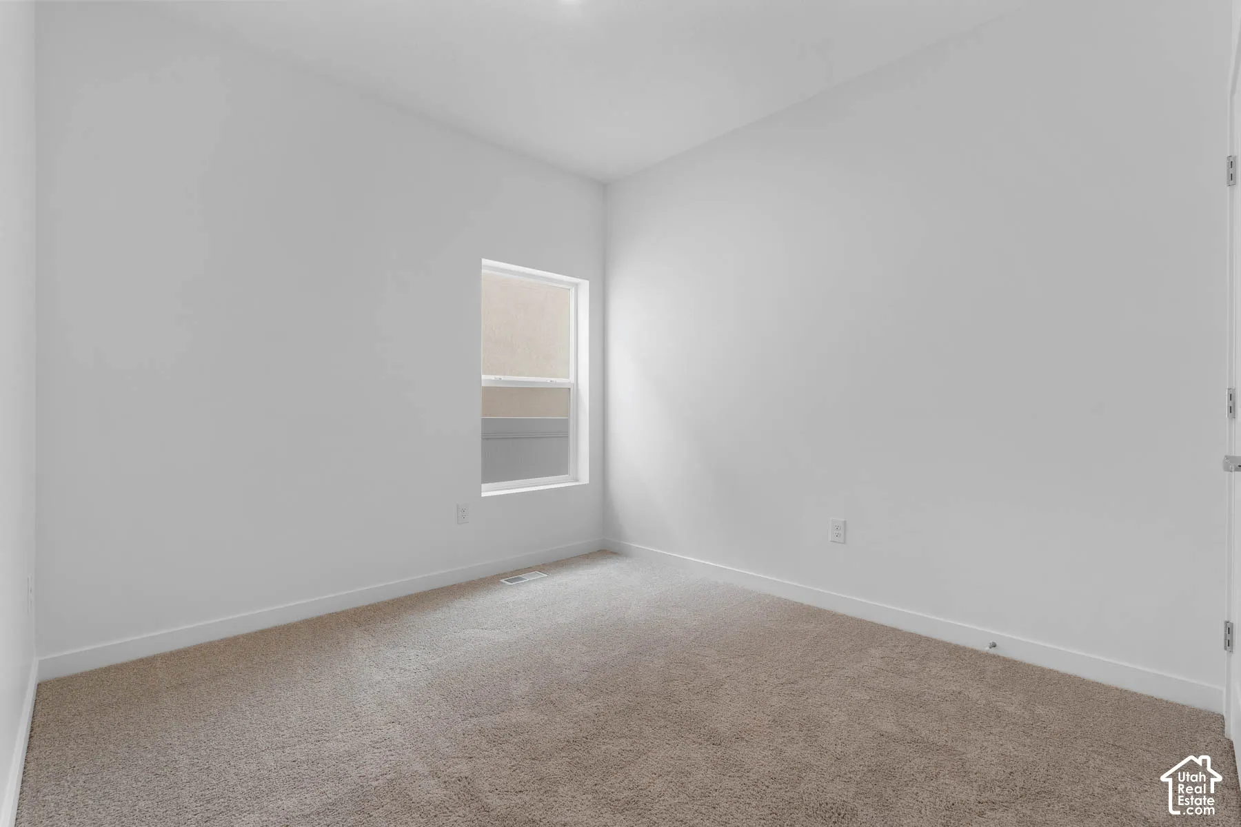 Neutral wall tones, carpet flooring, a single window, and a white door frame